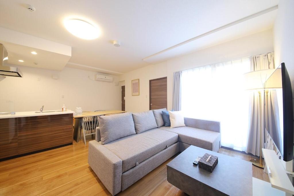 札幌市にある9min to Nishi 18 chome station up to 7ppl 3bed 1large sofa bedのソファとキッチンのあるリビングルーム