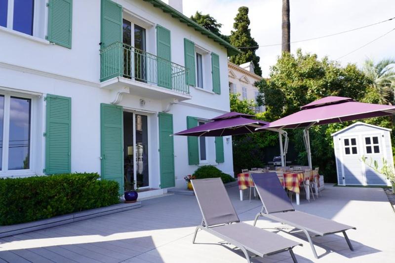 - deux chaises et des parasols sur une terrasse en face d'un bâtiment dans l'établissement Villa de charme, vue mer, baignée de soleil, à Grasse