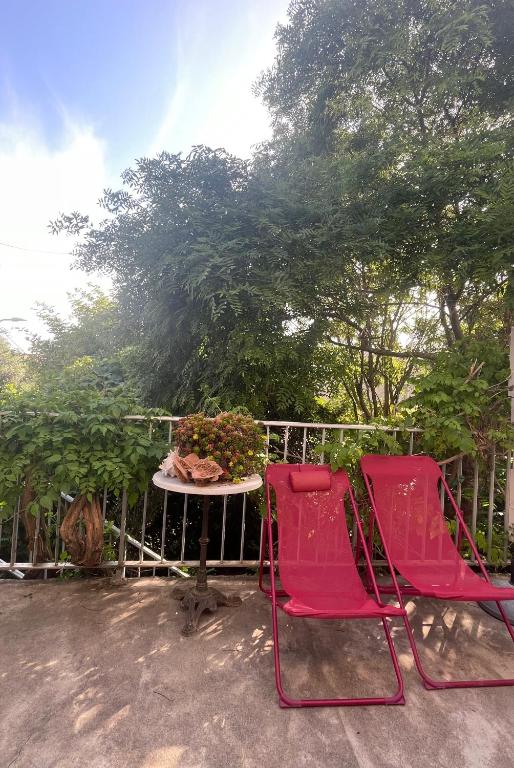 2 chaises rouges et une table sur une terrasse dans l'établissement Les jardins de Veronique Marie, à Mèze