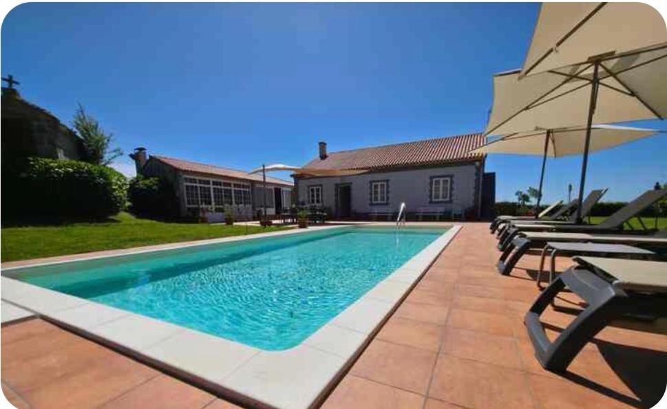 a swimming pool with chairs and an umbrella next to a house at Casa Emilia in Pontevedra