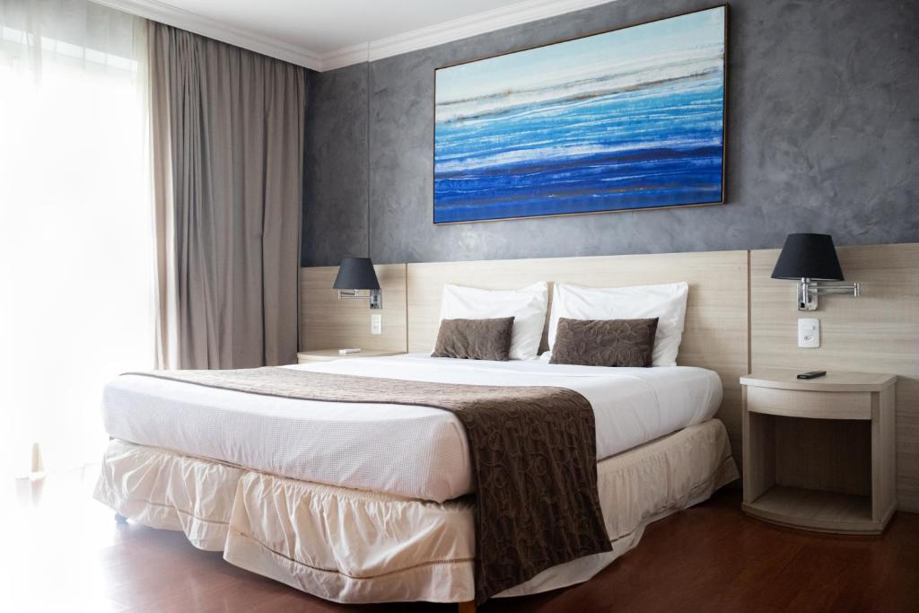 a bedroom with a large bed and a painting on the wall at BFC Suíte em Barra da Tijuca in Rio de Janeiro