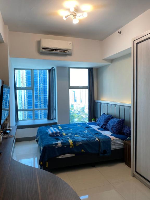 a bedroom with a bed with blue sheets and windows at Pakuwon Mall Apartemen Anderson Orchard Tanglin Benson by AquHome in Surabaya