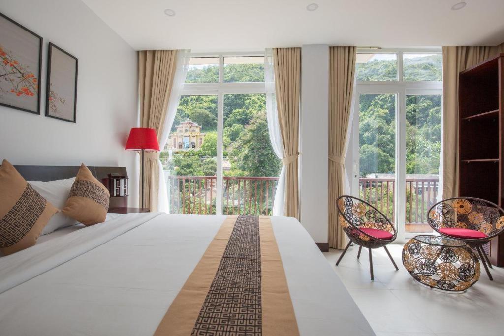 a bedroom with a large bed with two chairs and windows at Sea Mountain Hotel in Vung Tau