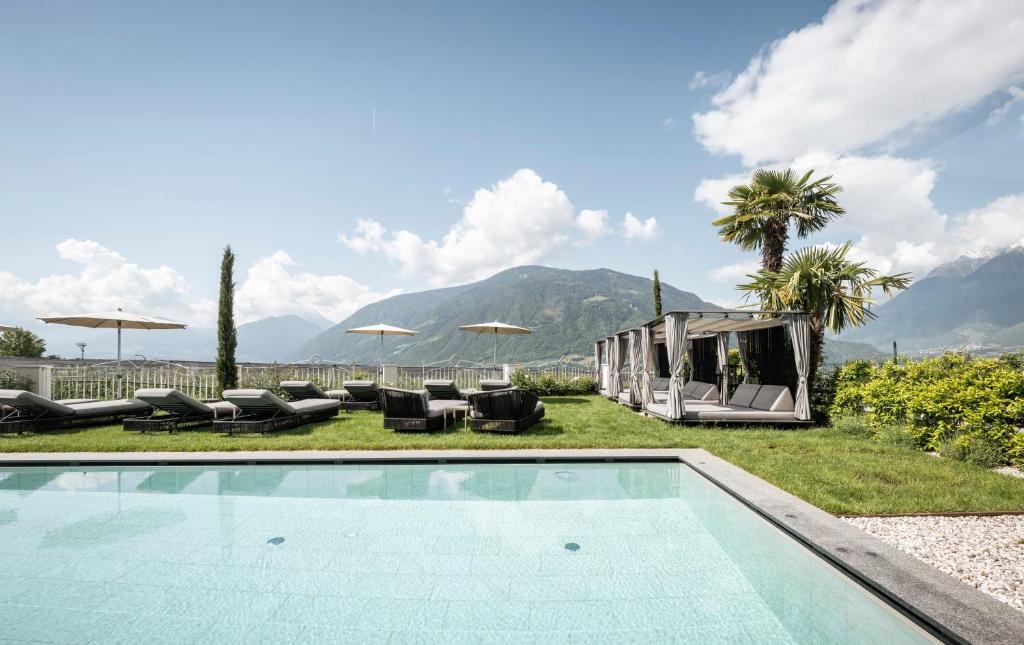 a swimming pool with chairs and umbrellas in a backyard at Small & Beautiful Hotel Gnaid in Tirolo