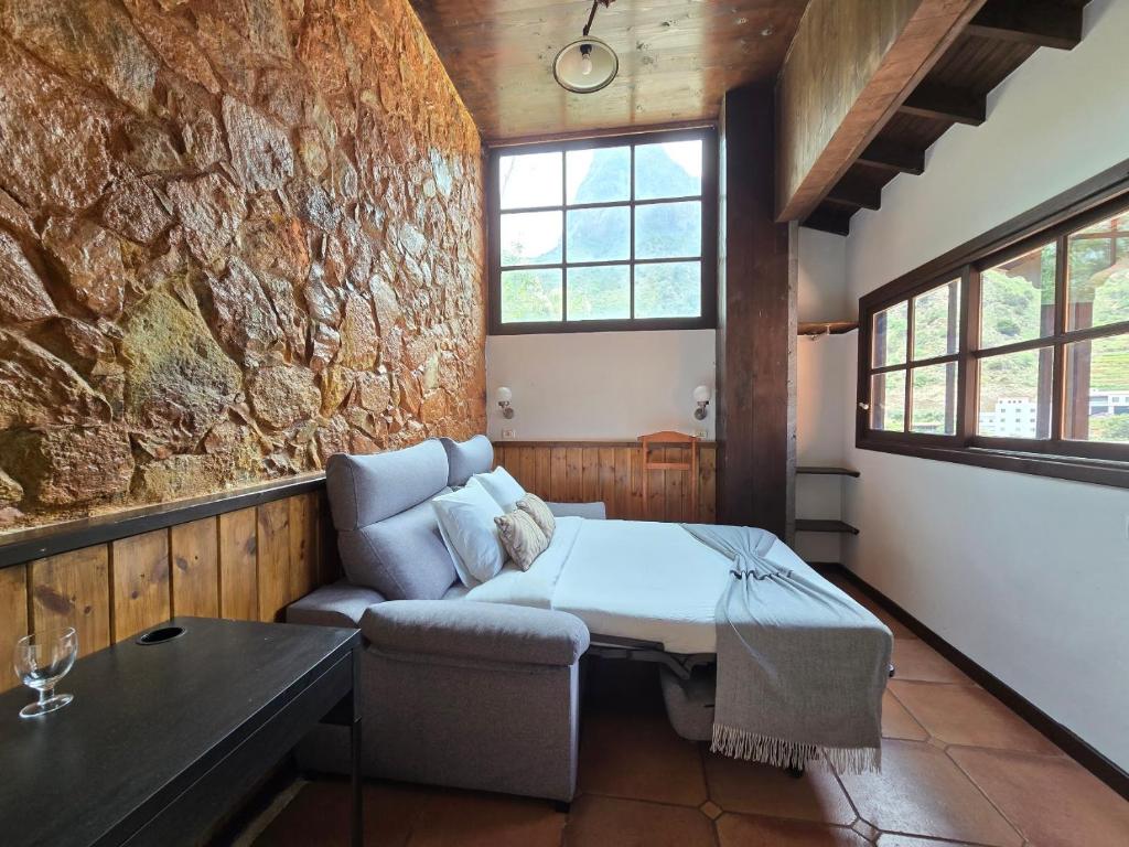 a room with a bed and a couch and a stone wall at Tamahuche Hotel Rural in Vallehermoso