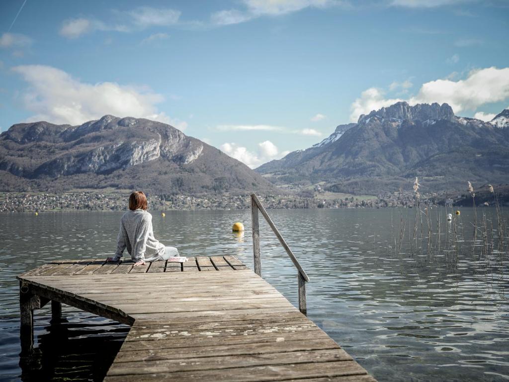 une femme assise sur un quai sur un lac dans l'établissement Venez Chez Vous - Aux Premières Loges Appartement Pieds dans l'eau, à Sévrier
