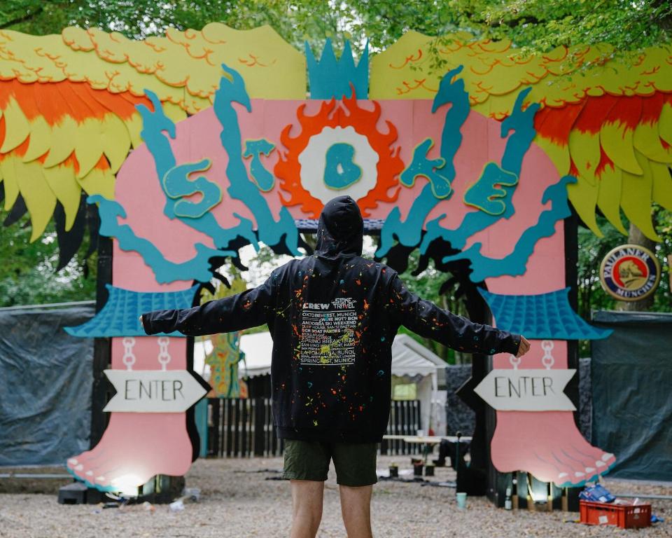 Un hombre está parado frente a un cartel colorido. en Oktoberfest and Springfest All-Inclusive Festival Camping, en Múnich
