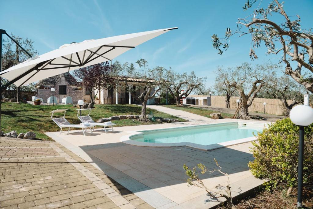 a swimming pool with a white umbrella over it at TRULLO MALVISCHI - Privacy & Pool in Alberobello