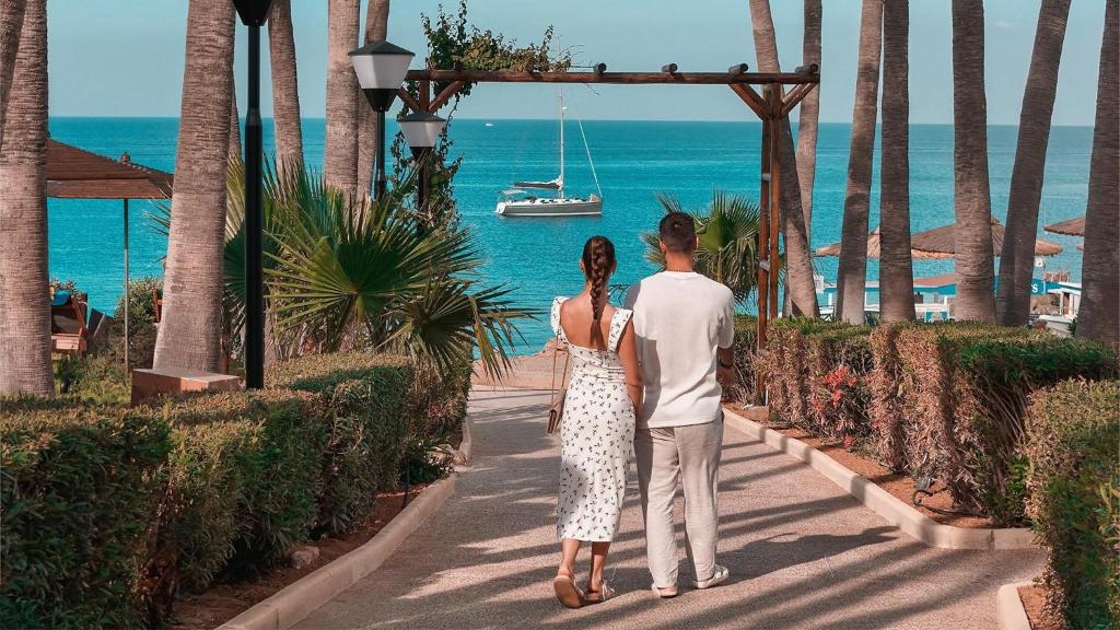 a man and woman walking down a walkway looking at the ocean at Cavo Maris Beach Hotel in Protaras