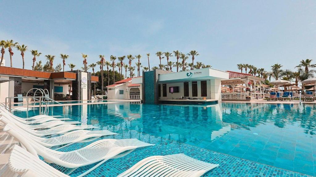 a large swimming pool with white chairs and palm trees at Cavo Maris Beach Hotel in Protaras