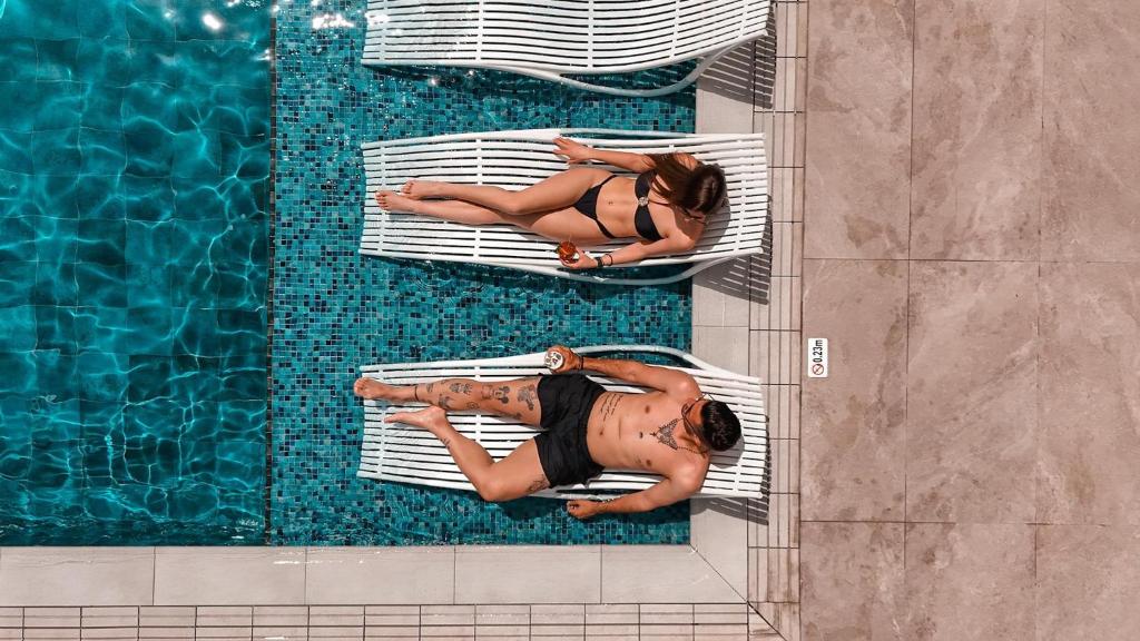 two women laying on beds next to a swimming pool at Cavo Maris Beach Hotel in Protaras