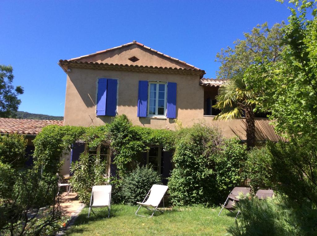 a house with blue shutters and chairs in the yard at Clos des Iris in Moustiers-Sainte-Marie