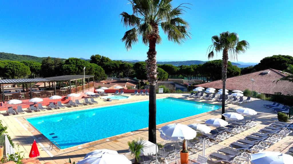 - une piscine bordée de parasols, de chaises et de palmiers dans l'établissement Village Vacances de Ramatuelle - Le Sentier des Pins, à Saint-Tropez