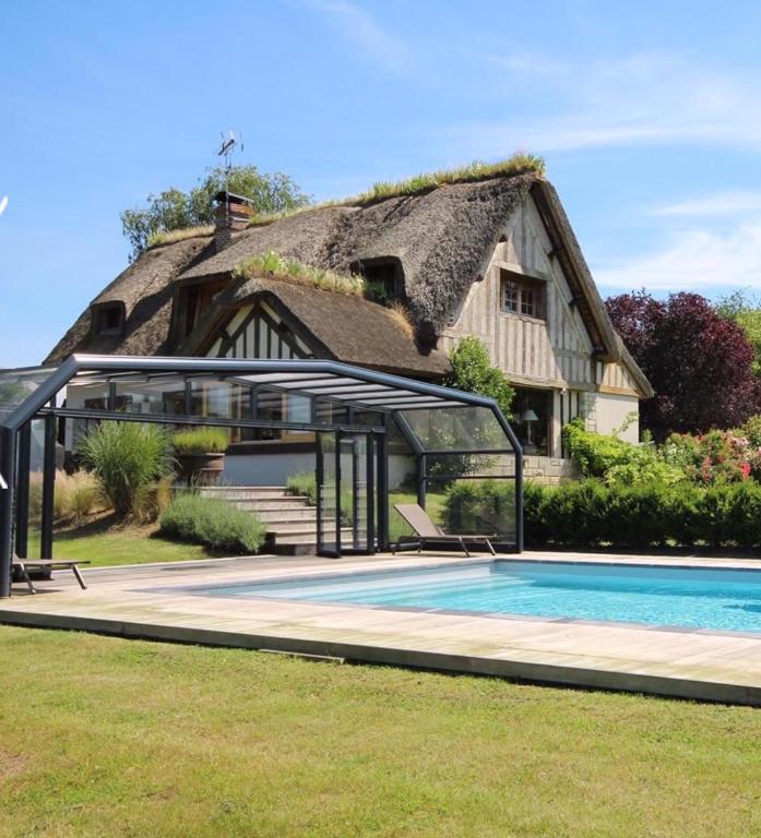 une maison avec un toit de chaume et une piscine dans l'établissement Chaumière de charme avec piscine, à Tourgéville