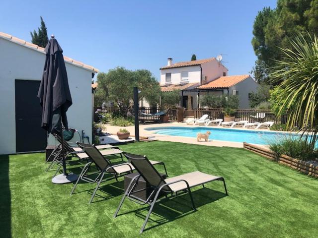 une cour avec des chaises, un parasol et une piscine dans l'établissement Les Oliviers, à Villemoustaussou