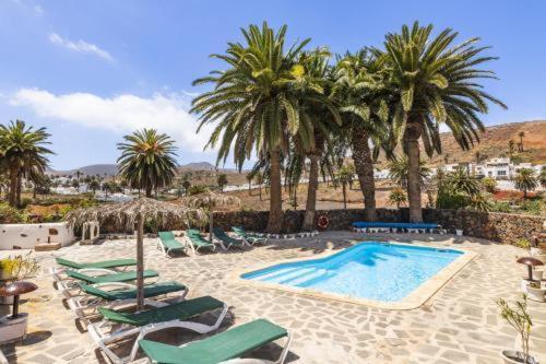 a swimming pool with lounge chairs and palm trees at Finca La Crucita - Órzola in Haría
