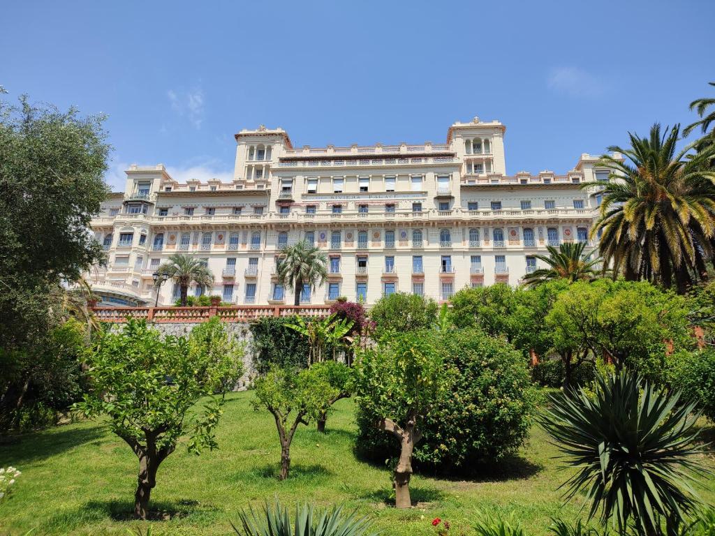 un grand bâtiment blanc avec des arbres devant lui dans l'établissement Appartement Riviera Palace, à Menton