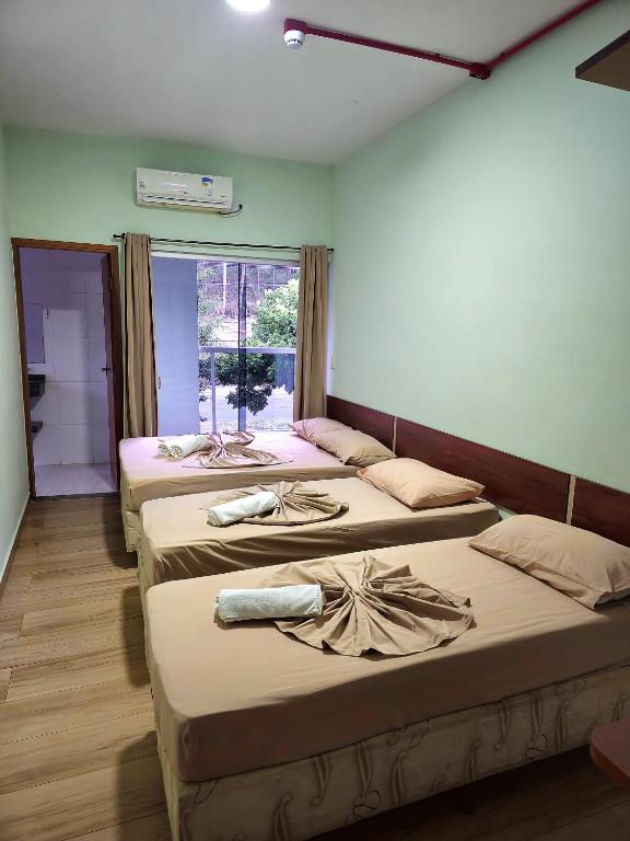 three beds in a room with a window at Pousada Monte Oliveira in Aparecida