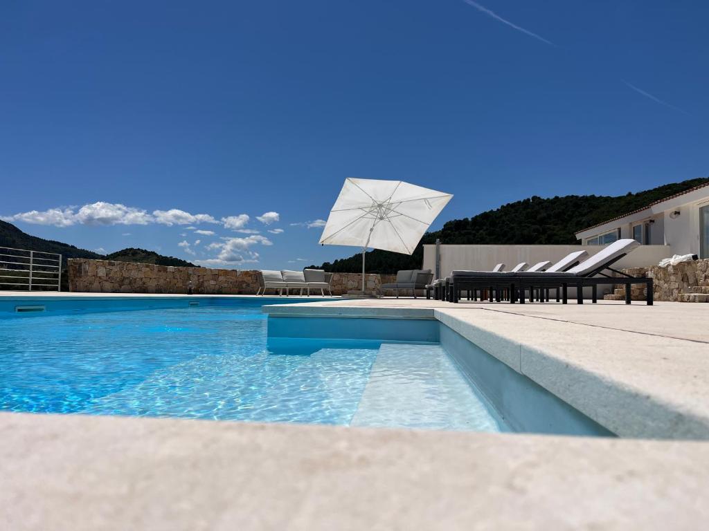 a swimming pool with two chairs and a white umbrella at Villa Mbita Sardegna in Brunella