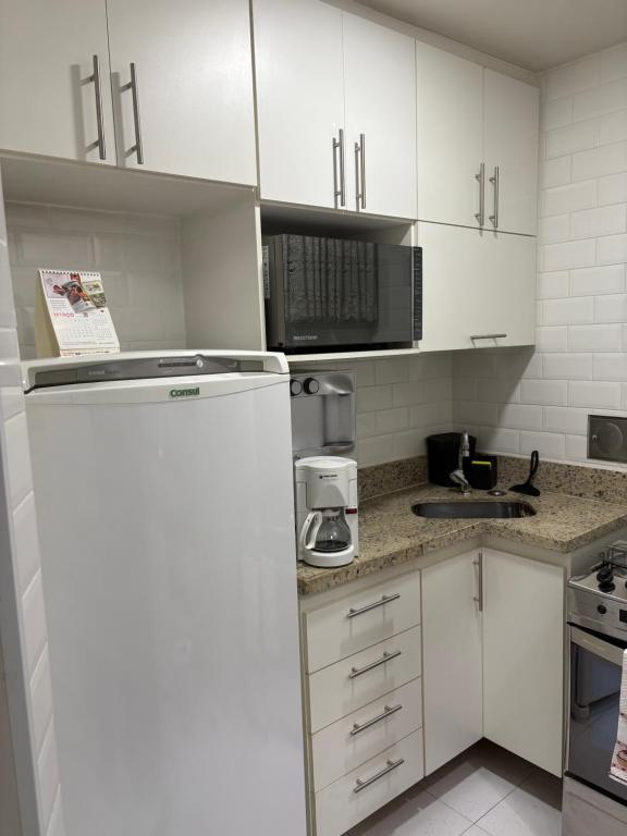 Una cocina con gabinetes blancos y un refrigerador blanco. en Aconchego Constante, en Río de Janeiro
