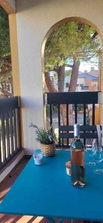 une table bleue avec une bouteille d'alcool sur un balcon dans l'établissement Camargue Village 2 Clim Balcon, au Grau-du-Roi