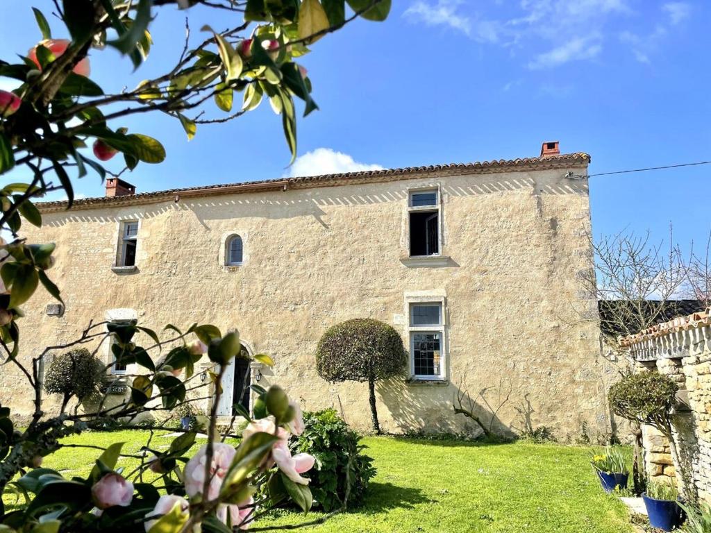 un vieux bâtiment en pierre avec une cour verte dans l'établissement Logis de la Vau - Private pool - Quiet, à Saint-Benoist-sur-Mer