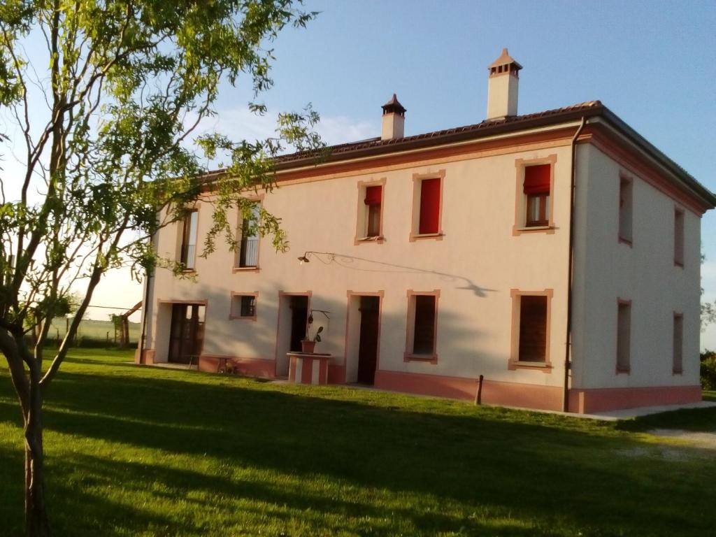 a large white building with red windows on a grass field at Antico Casale dei Sogni agriturismo in Lugo