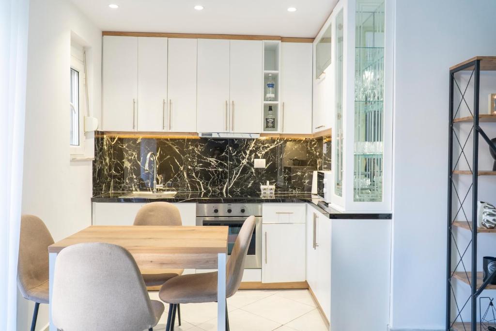 a kitchen with white cabinets and a wooden table and chairs at Mato Luxury Apartments 3 in Sarandë