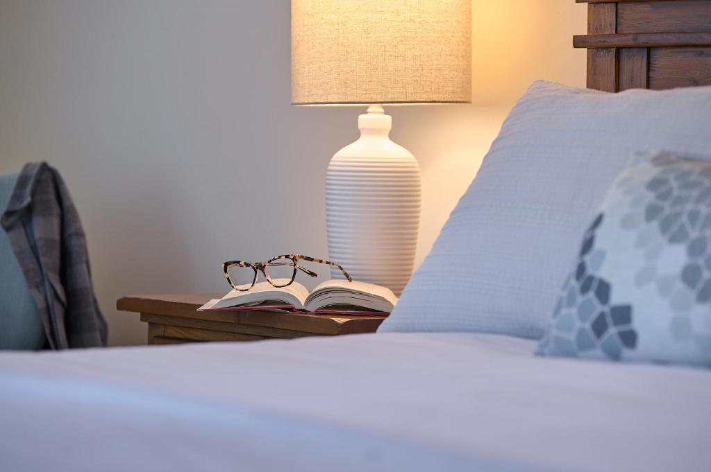 a bed with a lamp and a book and glasses on a table at Liahona Guest House in Ucluelet