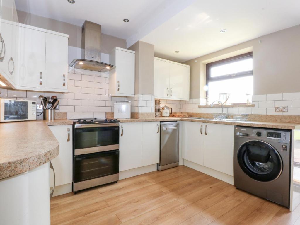 a kitchen with white cabinets and a washer and dryer at Fairfield in Pwllheli