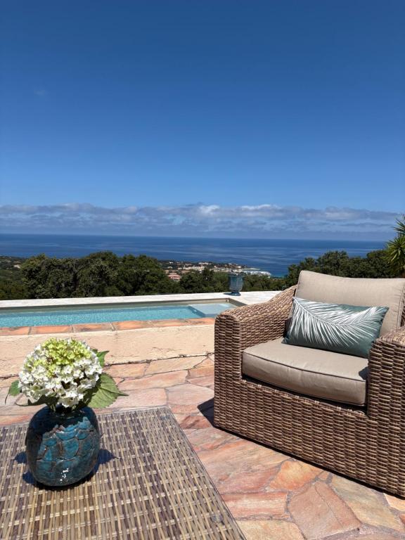 une chaise en osier et un vase avec des fleurs sur une terrasse dans l'établissement LUMIO Élégance & Calme absolu avec piscine et vue mer, à Lumio