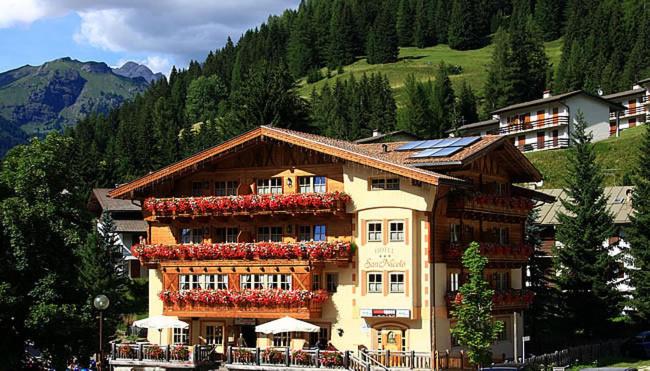 a large building with red flowers on it at Hotel Garni San Nicolò in Pozza di Fassa