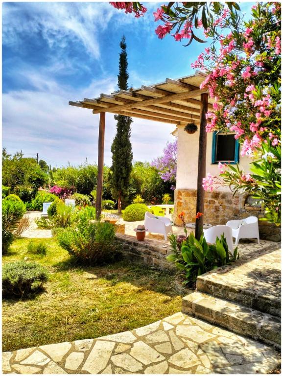 a garden with a wooden pergola and white chairs at Lemon Tree Cottage in Finikounta