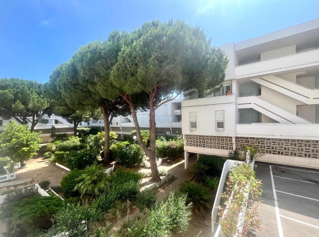 un immeuble d'appartements avec un arbre devant dans l'établissement Antinéa - Clarté, Calme et Confort à 200m de la Plage avec Parking, à La Grande Motte
