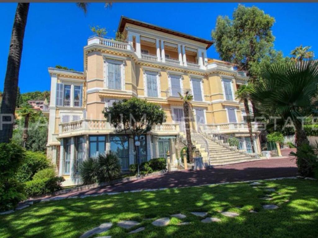 une grande maison jaune avec des palmiers devant elle dans l'établissement Calme 2P avec terrasse et jardin, parking et piscine - FR-1-196-382, à Menton