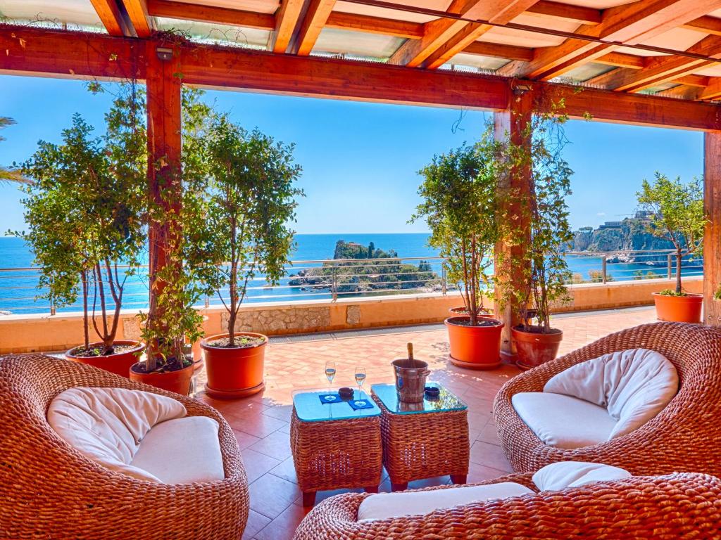 a patio with wicker chairs and tables and a view of the ocean at Taormina Panoramic Hotel in Taormina