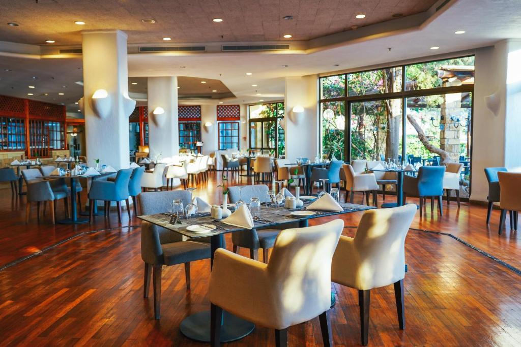a dining room with tables and chairs and windows at Coral Beach Hotel & Resort Cyprus in Coral Bay
