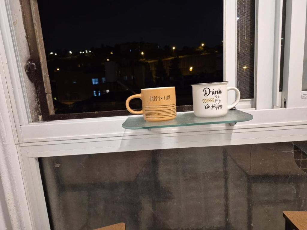 エルサレムにあるJerusalem apartmentの窓辺に座るコーヒーマグカップ2つ