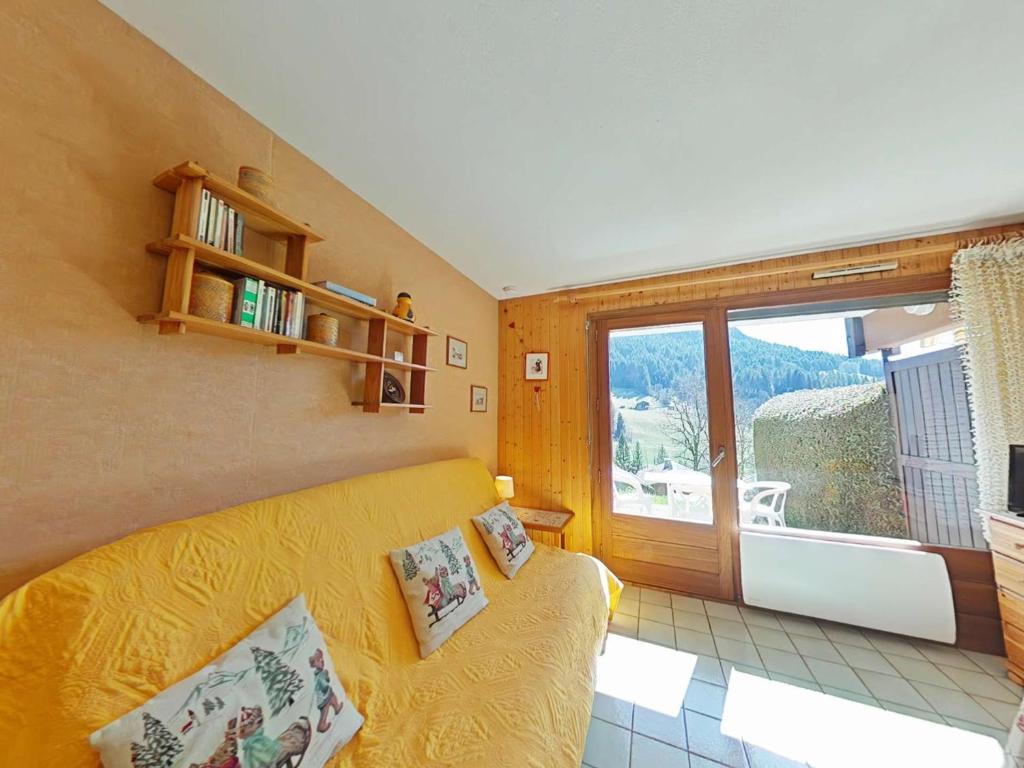 - un salon avec un canapé jaune et une grande fenêtre dans l'établissement Studio cosy avec terrasse sud, proche navettes, Le Grand-Bornand - FR-1-241-51, au Grand-Bornand