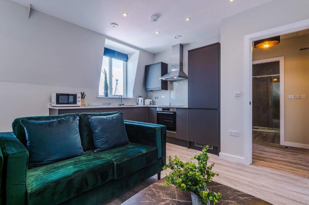 a living room with a green couch and a kitchen at Elysée Suites - Chic 1 Bed Flat in Southport in Southport