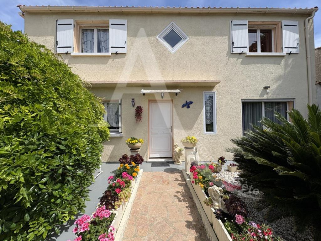 une maison blanche avec des fleurs devant elle dans l'établissement Maison 6 personnes, salon climatise, wifi et stationnement, à Sète