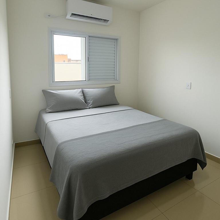 a bed in a white room with a window at Apto Novo com Ar e Wi-Fi Perto da UFU Monte Carmelo in Monte Carmelo