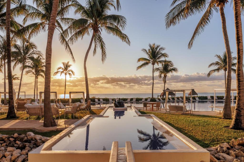 Una mujer está parada frente a una piscina con palmeras. en Paraiso de la Bonita Adult All-Inclusive, a Luxury Collection Resort, en Puerto Morelos