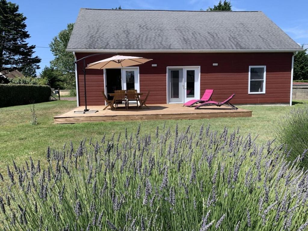 une petite maison rouge avec des chaises roses et un parasol dans l'établissement The Red House near the beach, à Denneville-Plage