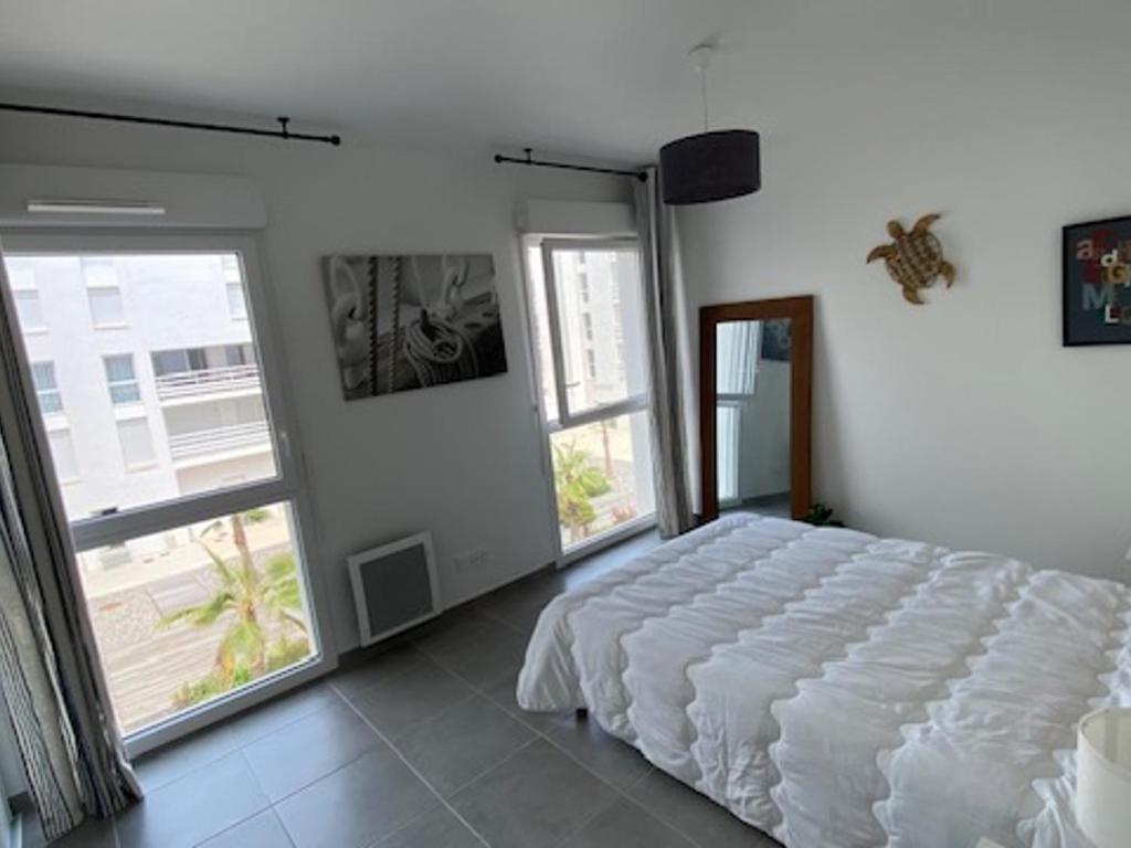 sypialnia z białym łóżkiem i dużymi oknami w obiekcie Superbe T2 Climatisé avec Terrasse - 4 Pers, Ascenseur, Parking Privé, à 400m de la Plage - FR-1-727-15 w mieście Port Leucate