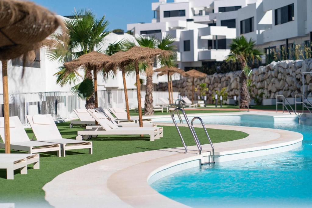 ein Swimmingpool mit Liegestühlen und Sonnenschirmen in einem Ferienresort in der Unterkunft Serena Village beautiful 3 bedroom terraced house close to the beach in La Cala de Mijas