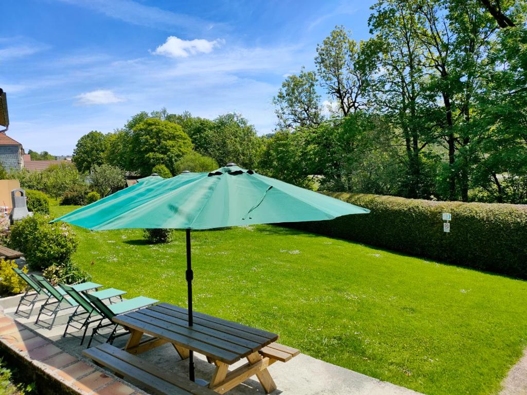 a picnic table with a blue umbrella in a yard at Gîte 295 Montagnes du Jura avec Spa et Sauna classé 3 étoiles in Foncine-le-Haut