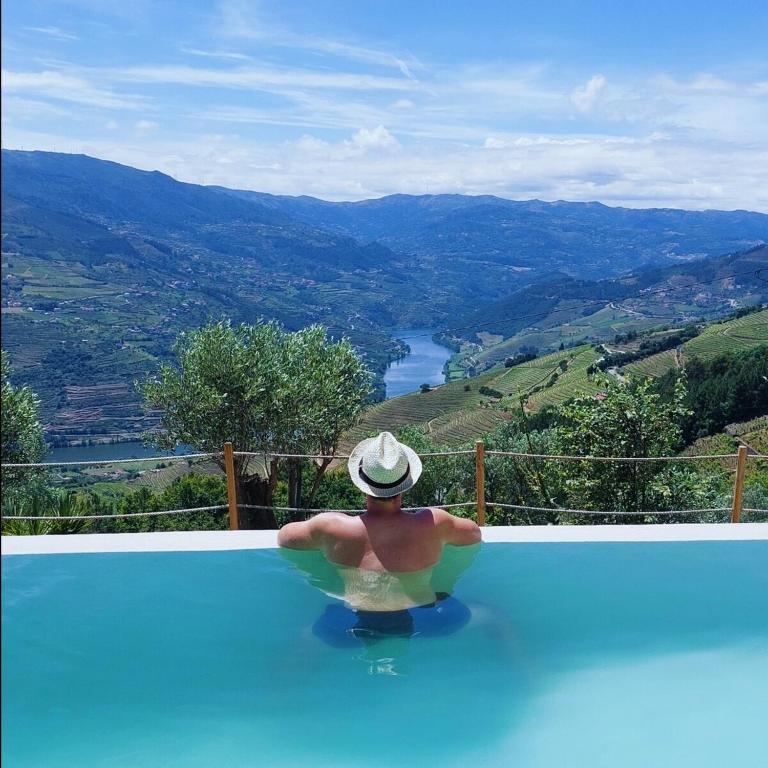 a man sitting in a swimming pool with a view at Retiro Vale do Douro in Vila Marim