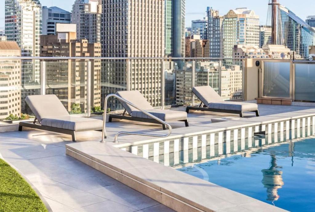 a rooftop pool with lounge chairs and a city skyline at Stylish Family 1BR with Cozy Bunks and Games for 5 in Sydney