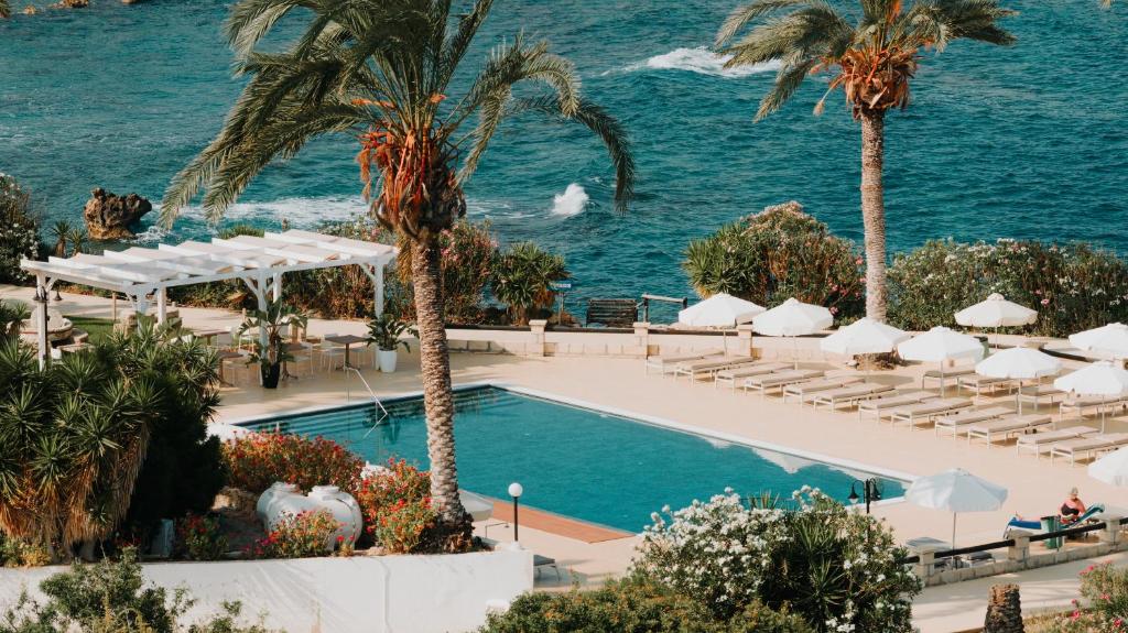 a pool at a resort with palm trees and chairs at Vrachia Beach Hotel & Suites - Adults Only in Paphos